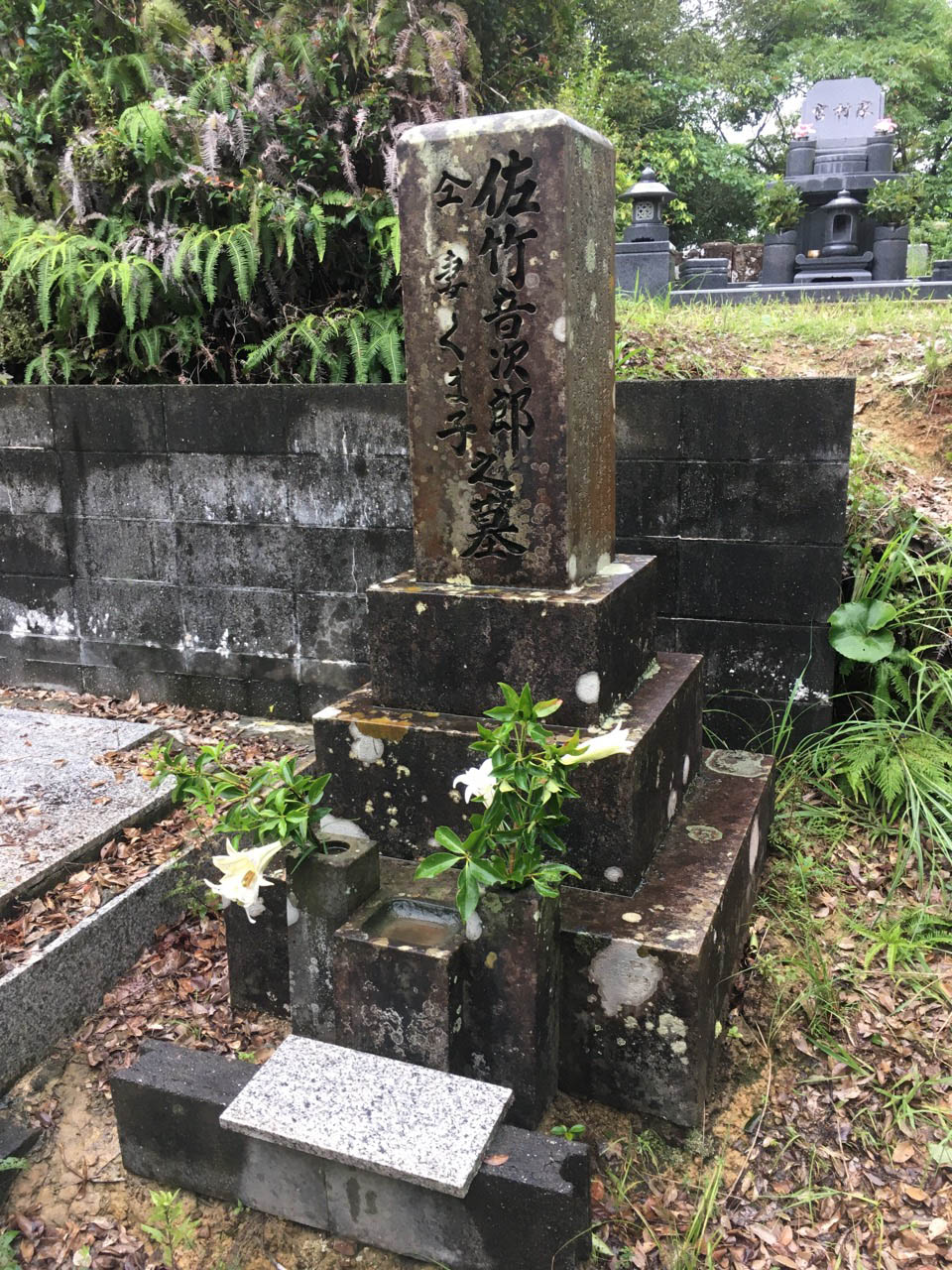 音次郎竹島墓地の墓石の写真。雨に濡れている。榊と野の百合が生けられている。