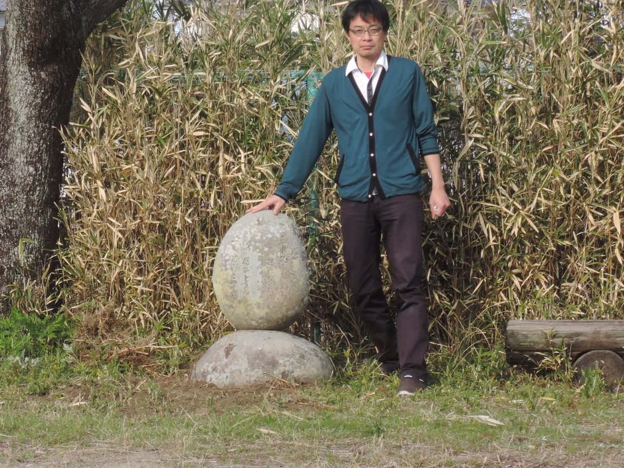 移転が完了した辞世の句碑。作業に立ち会った事務局瀬戸雅弘と並んで大きさの比較をする。石碑は腰の高さほど。モデルの身長は約180cm