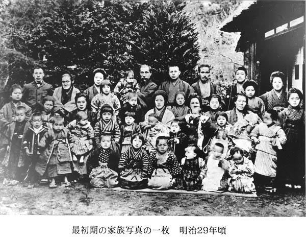 最初期の家族写真の一枚。明治35年頃。腰越医院の中庭。右手に増築された小児保育院らしき建物が見える。鬱蒼とした庭木の前で38人の大人と子どもが整列している。