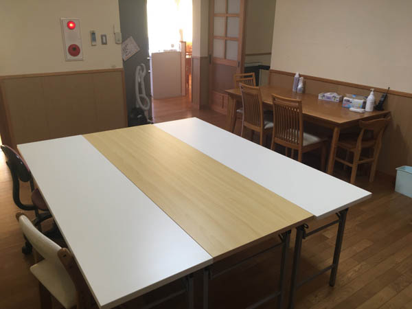 音次郎会資料室のある若草園西住居棟１階に設置された会議テーブル。白木調の木目テーブルの両側を白のテーブルがはさんでいる。