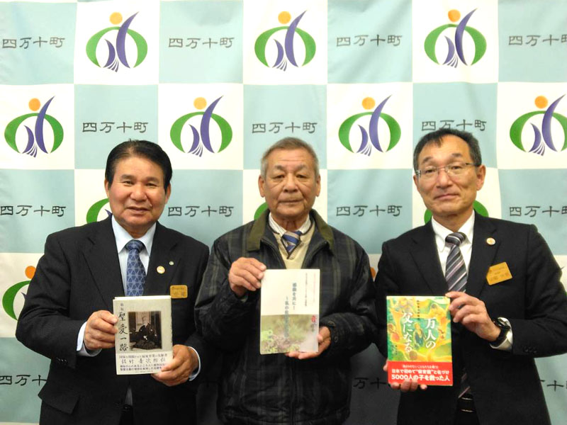 寄贈された3種類の伝記を披露する中平会長（中央）